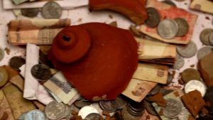 Indian style piggy bank mad of mud broken with money spread around it.